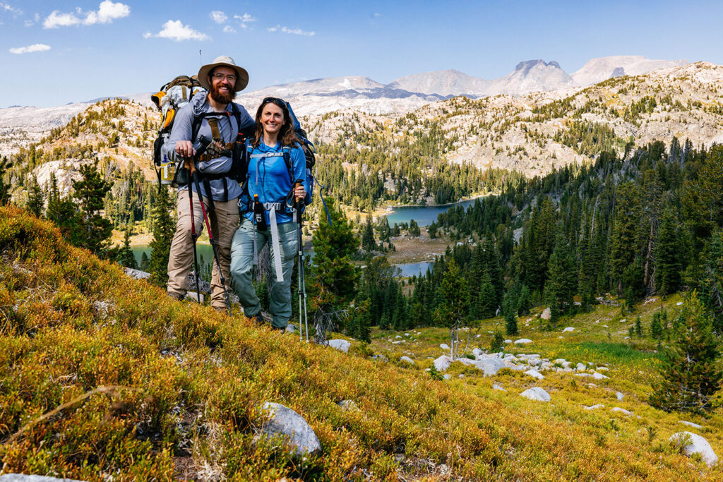 Two hikers standing above an alpine lake with mountain views in Montana during summer