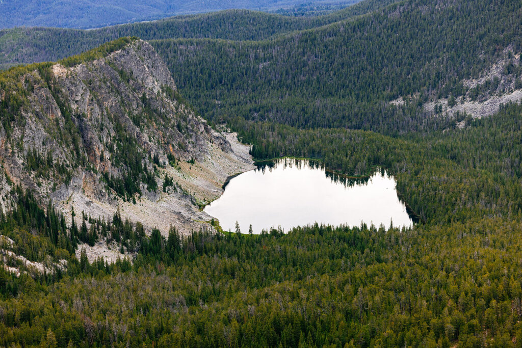 View of an alpine lake tucked beneath cliffs in Montana after hiking to a ridge above camp on a return backpacking trip.