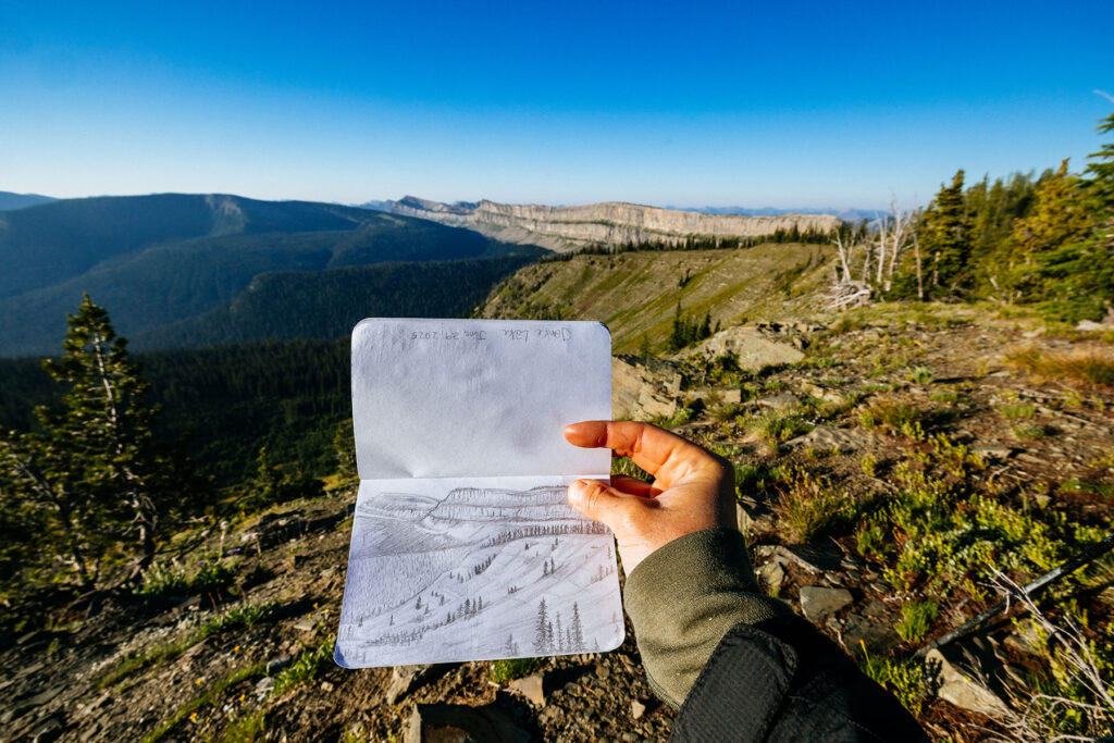 Sketchbook drawing of Montana's Chinese Wall held in front of the actual landscape during sunrise.