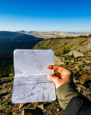 Sketchbook drawing of Montana's Chinese Wall held in front of the actual landscape during sunrise.
