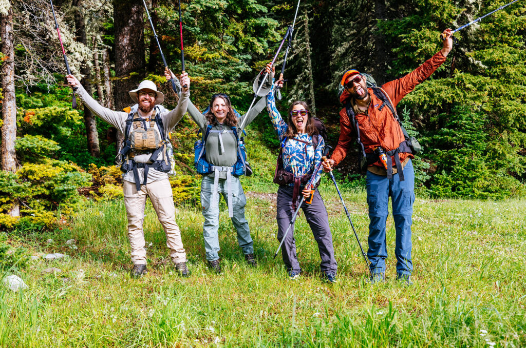 Group of four backpackers posing with trekking poles at the South Fork Teton Trailhead before beginning a five-day backpacking trip to Montana's Chinese Wall.